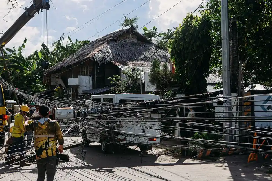 Workers fix tangled power lines after an accident involving a vehicle in a tropical location.